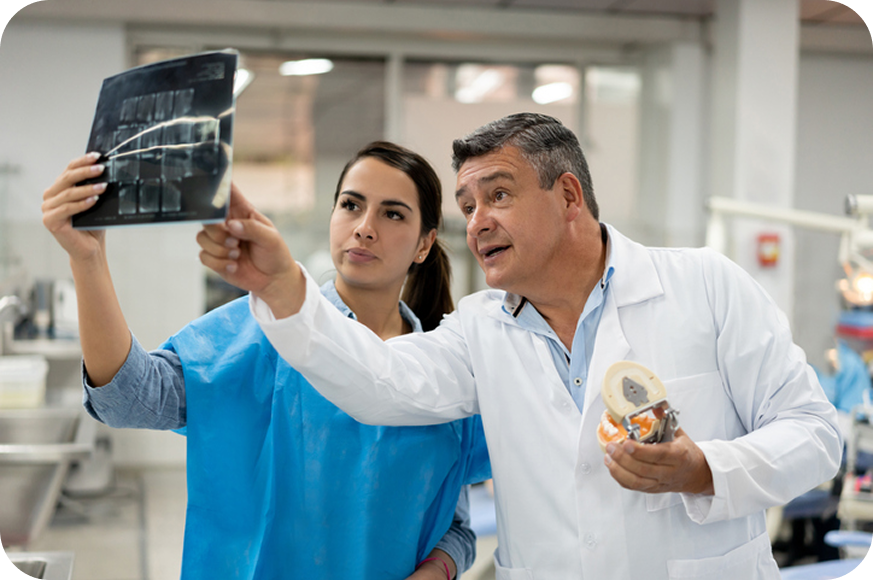 Two dental medical professionals, one holding an X-ray and the other a model, in a hospital setting.